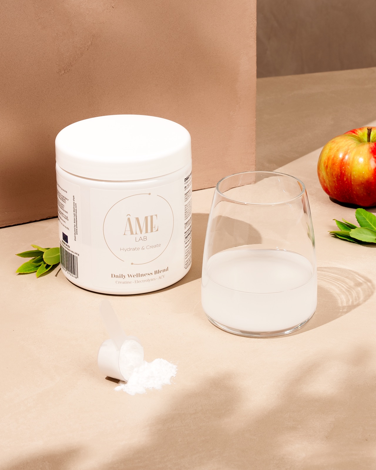 The jar beside a glass of water, a scoop of powder and an apple in soft morning light